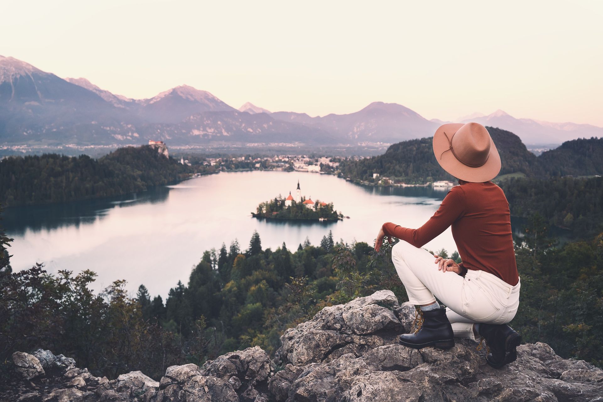 Una mujer con sombrero se sienta en una roca con vistas a un lago.