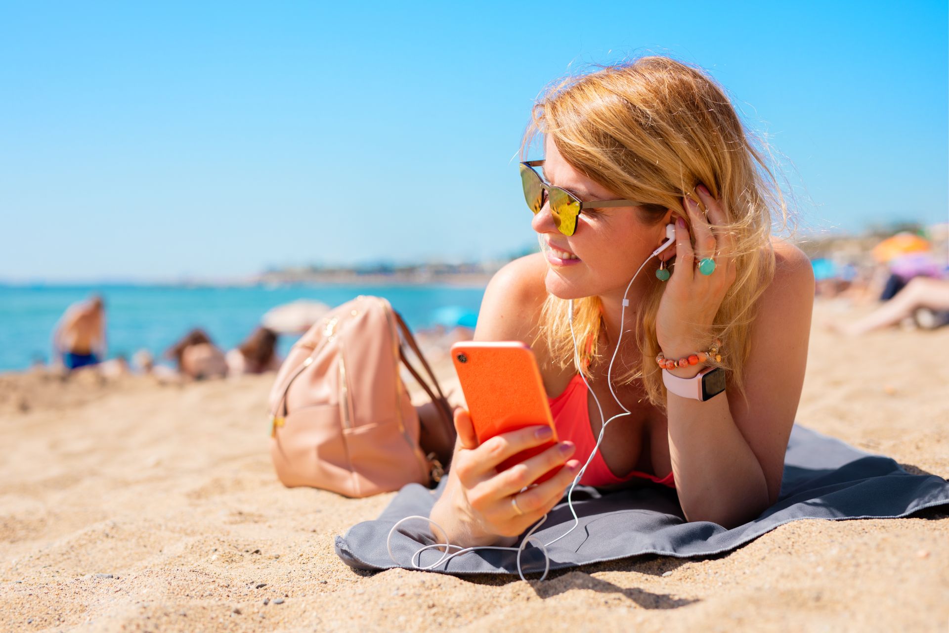Una mujer está tumbada en la playa escuchando música en su teléfono.