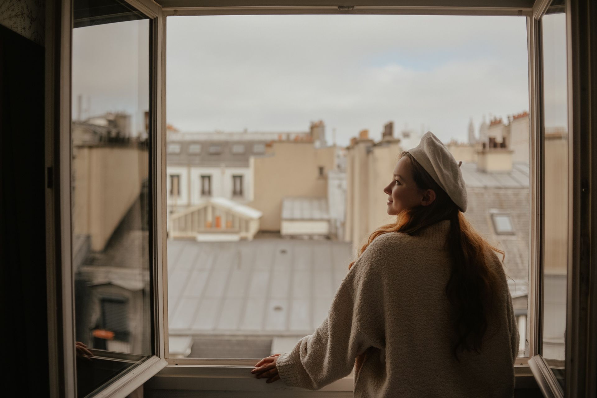 Una mujer con boina mira por una ventana abierta.