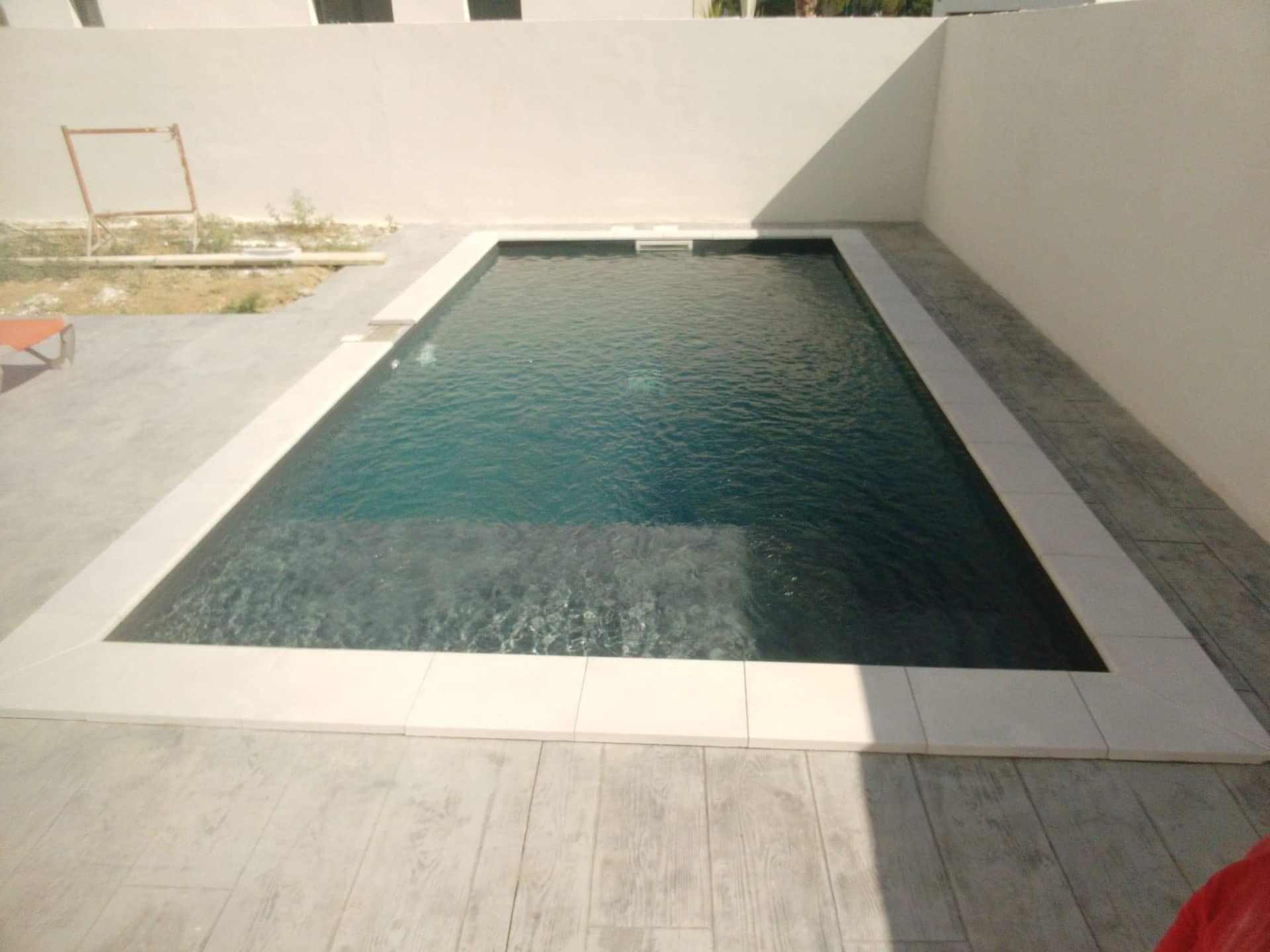 Piscine avec une terasse en carrelage et un contour blanc