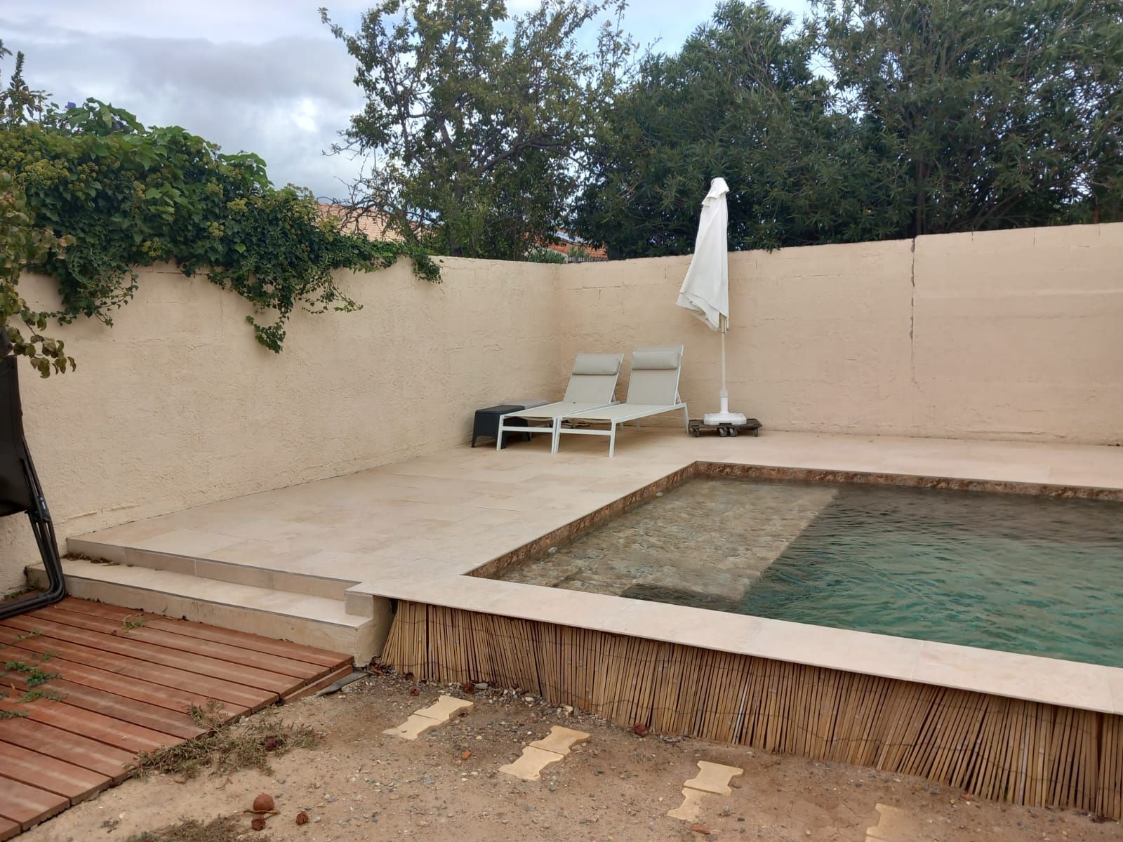 Piscine avec une terrasse en carrelage beige avec un transat et un parasol blanc