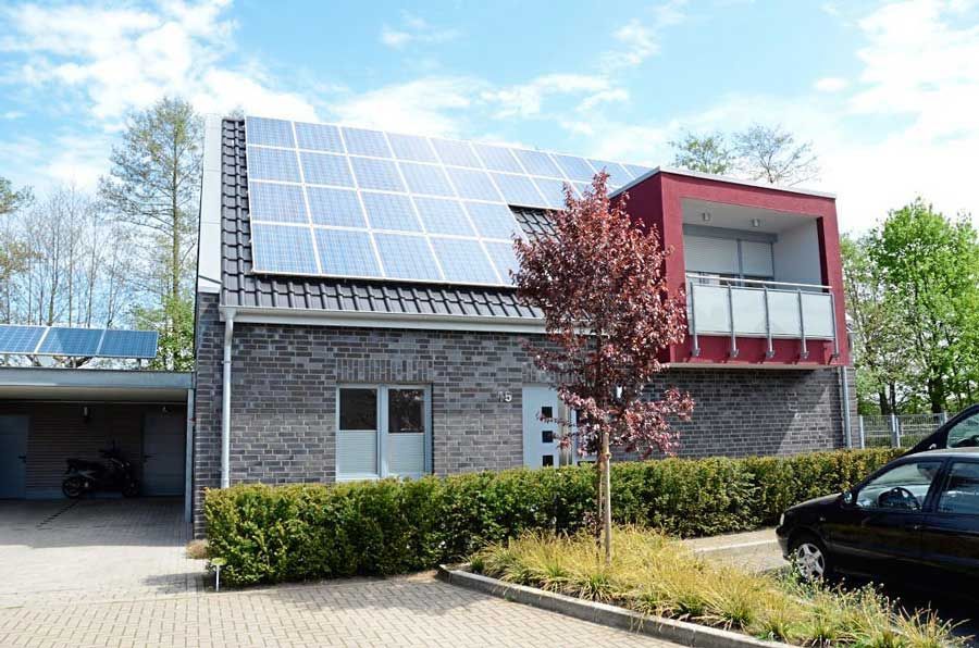Ein Haus mit Solarzellen auf dem Dach und einem davor geparkten Auto.