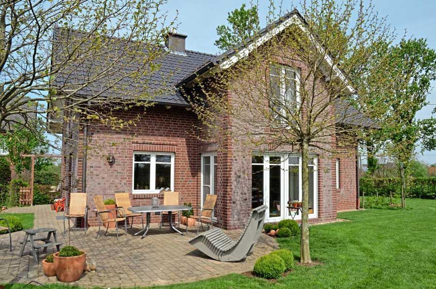 Ein großes Backsteinhaus mit einer Terrasse und Stühlen davor.