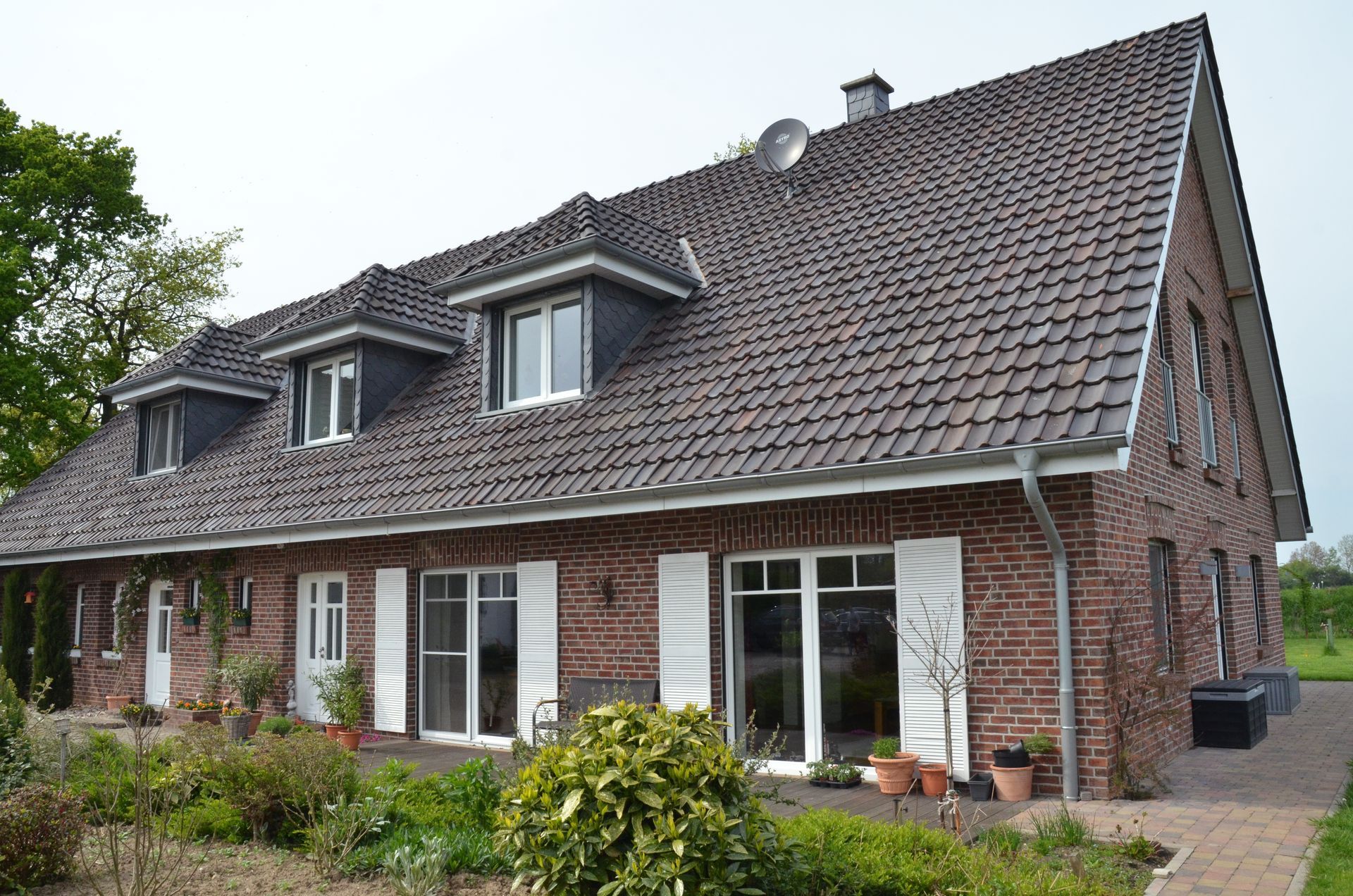 Ein großes Backsteinhaus mit grauem Dach und weißen Fensterläden