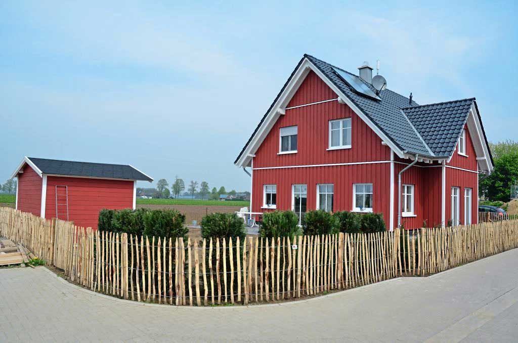 Ein rotes Haus im schwedischen Stil mit einem Holzzaun davor.