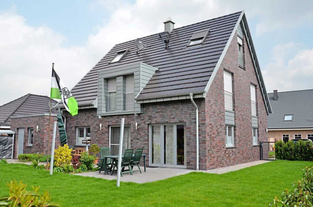 Ein großes Backsteinhaus mit grauem Dach und einer großen Wiese davor.