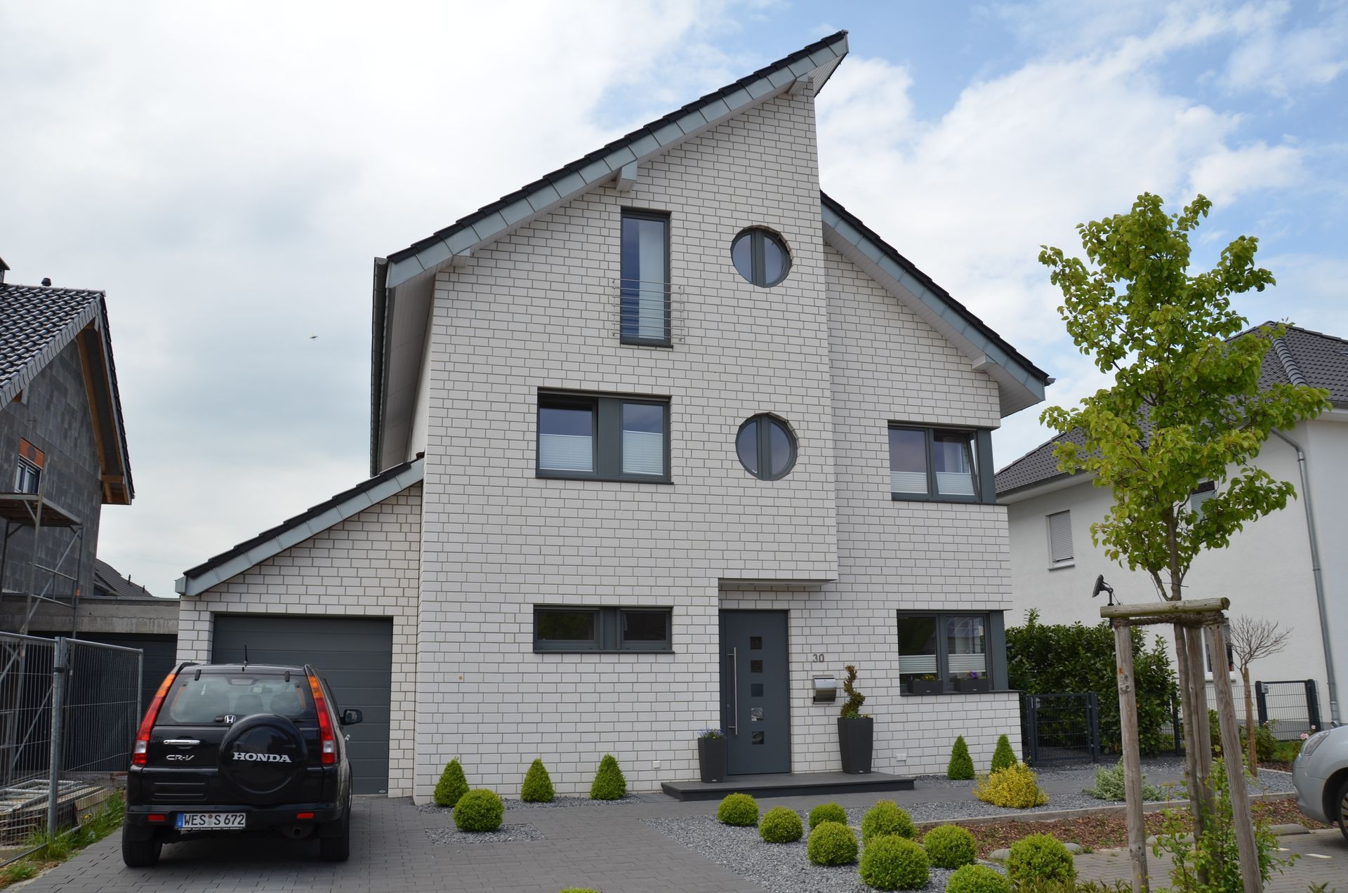 Vor einem weißen Backsteinhaus ist ein Auto geparkt.