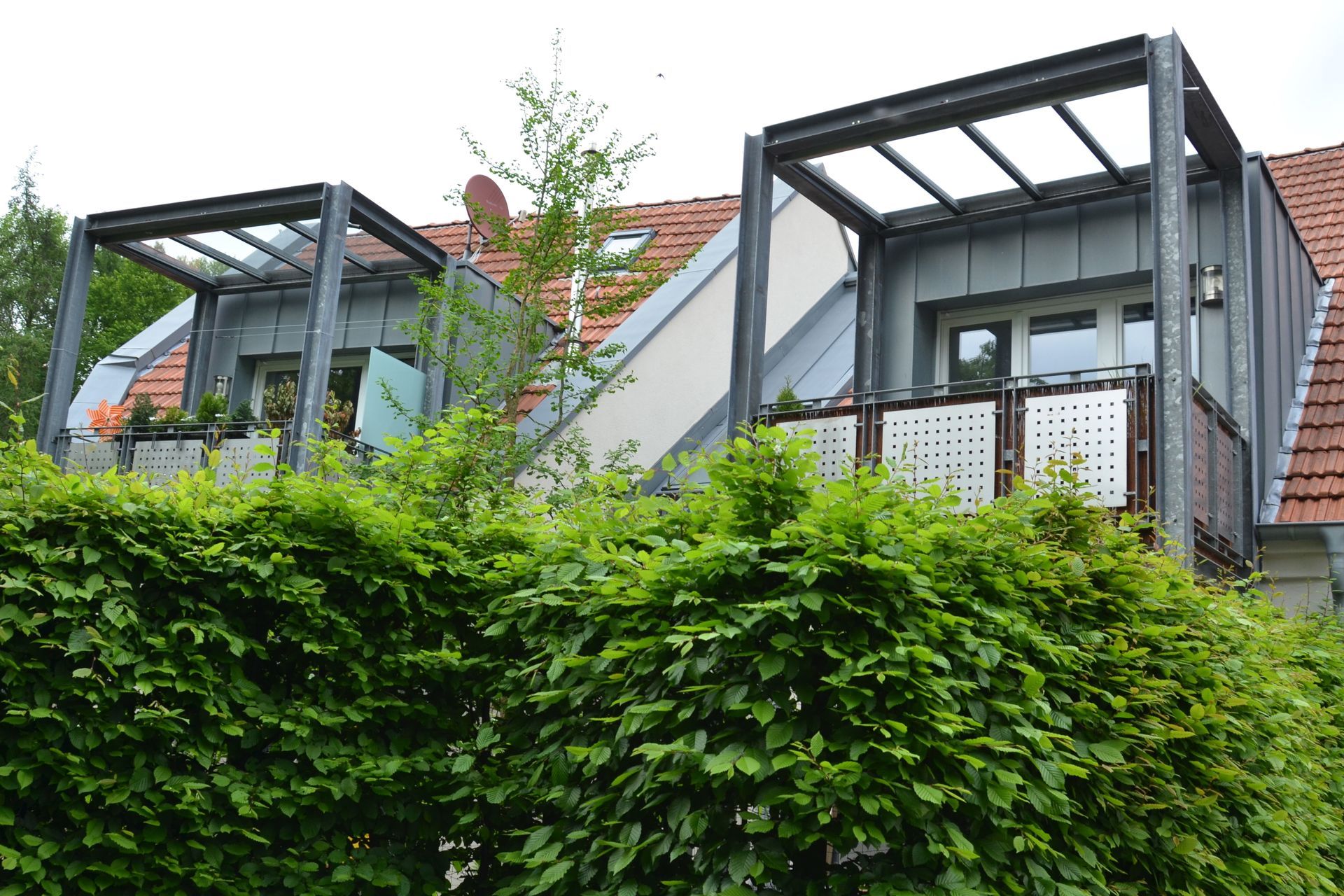 Ein Haus mit Balkon und einer Hecke davor