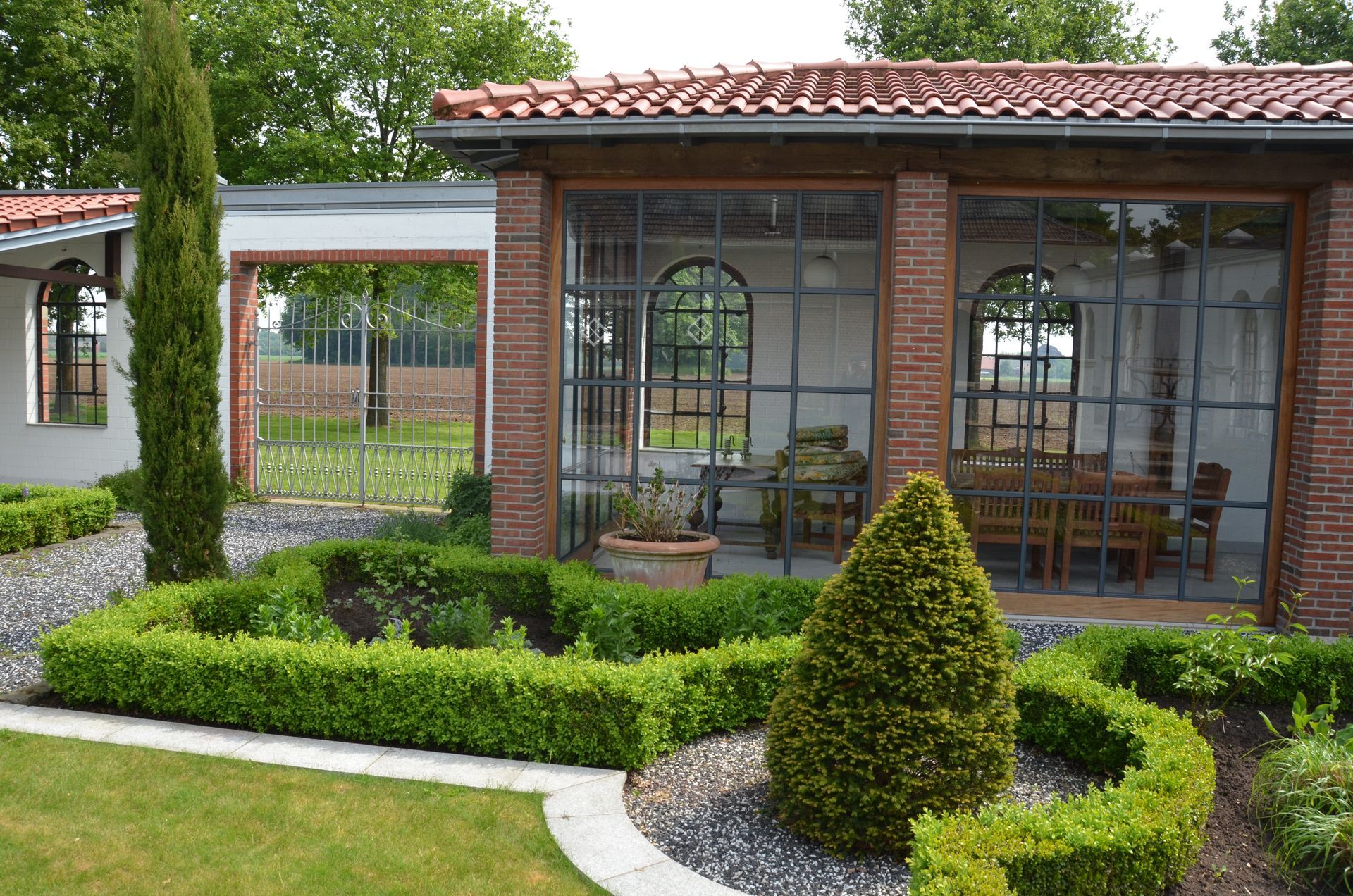 Ein Haus mit einem roten Ziegeldach ist von Büschen und Bäumen umgeben