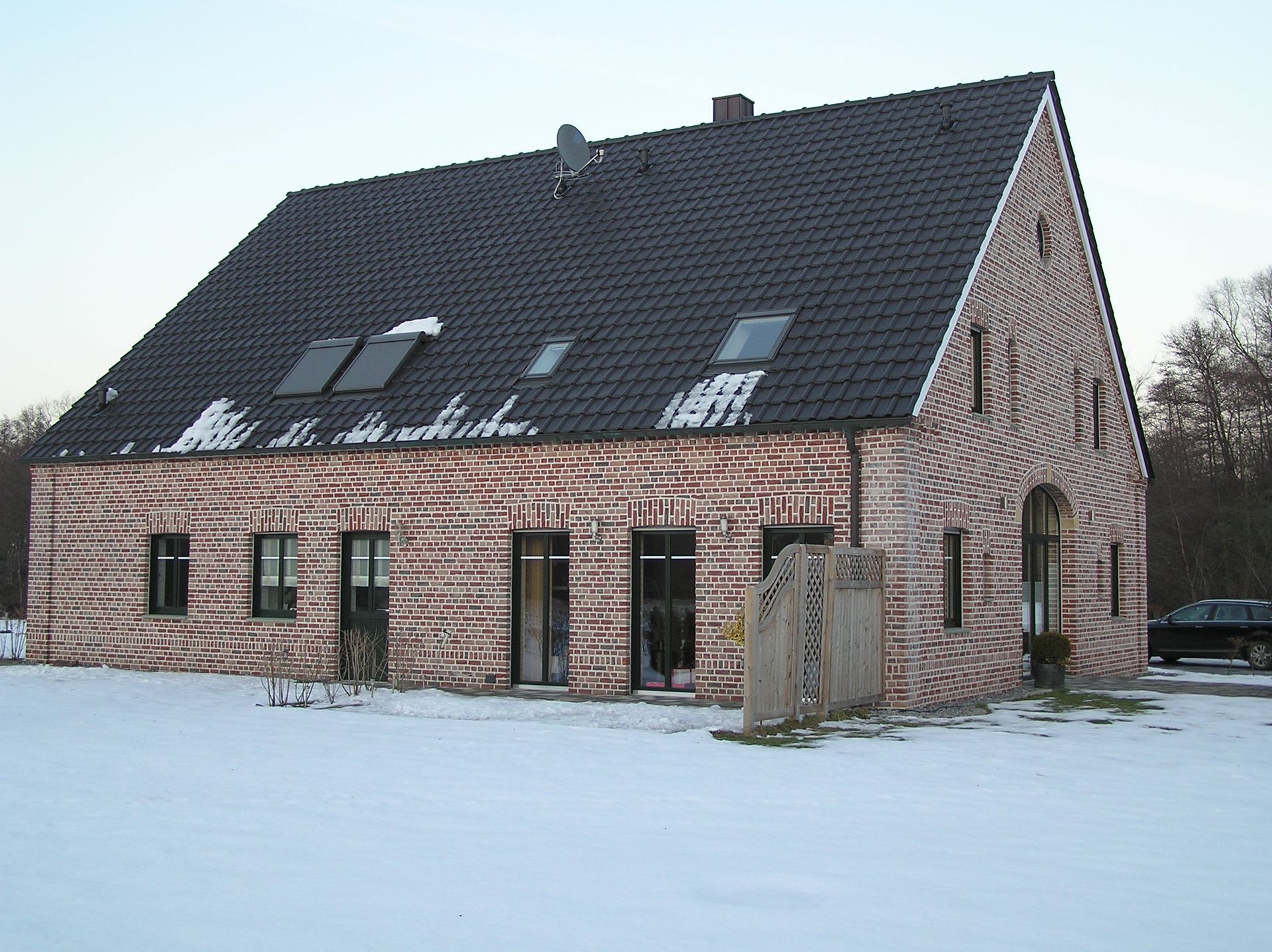 Ein Backsteinhaus mit schwarzem Dach ist von Schnee umgeben