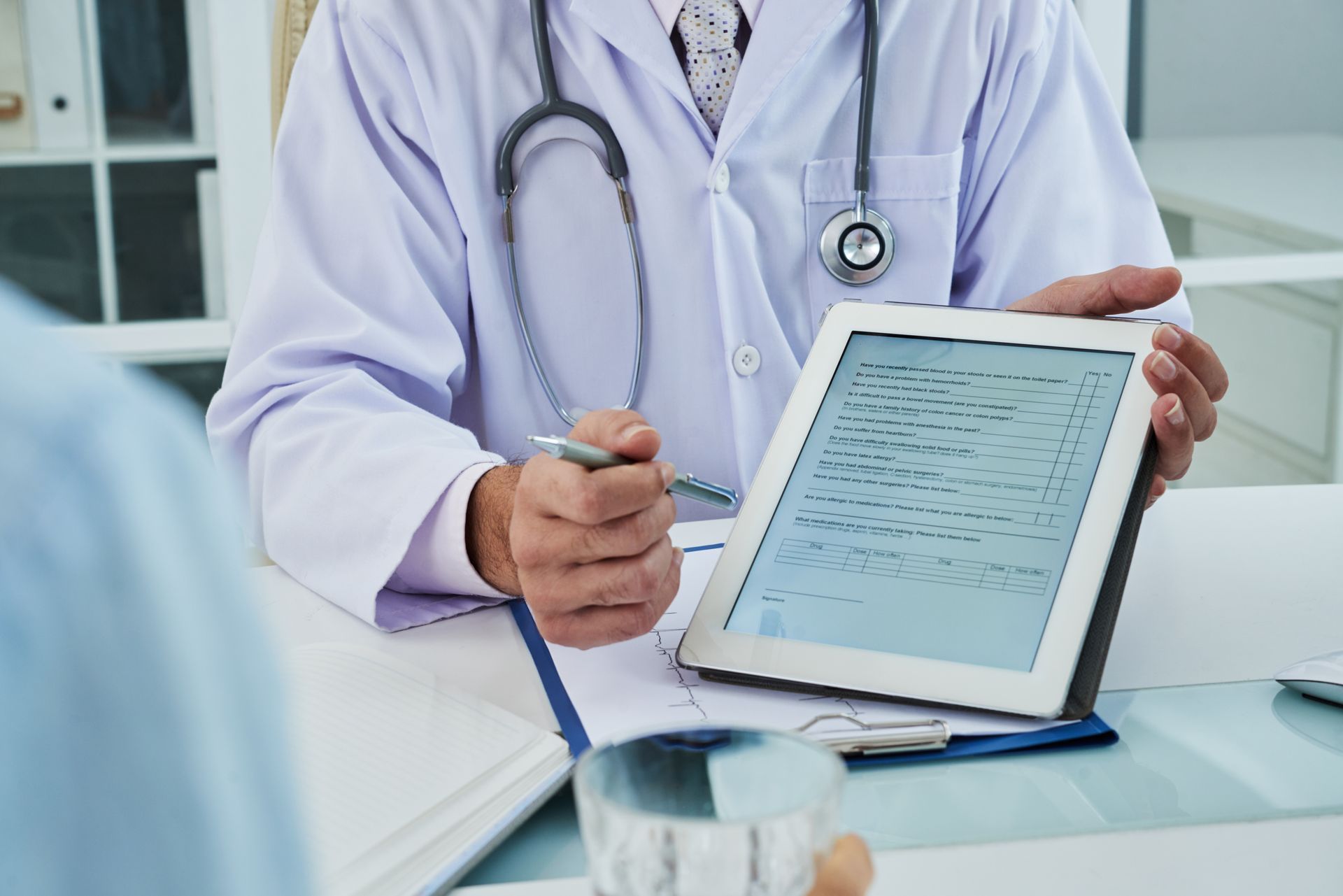 Médico sosteniendo una tableta con historiales médicos en un luminoso consultorio clínico.