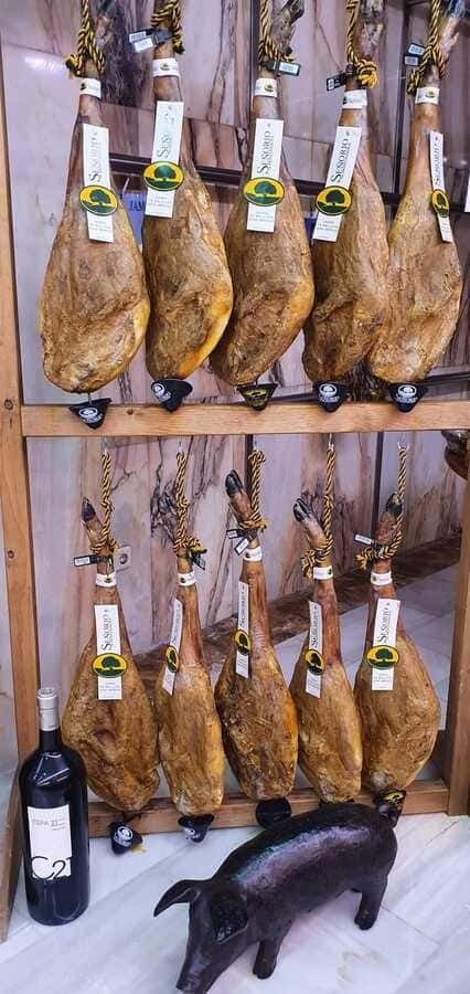 Una fila de jamones colgados en un estante junto a una botella de vino.