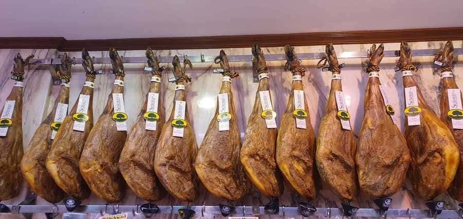 Una fila de jamones colgados en un estante en una tienda.