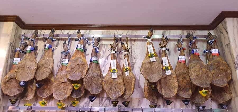 Un montón de jamones están colgados en un estante en una pared.