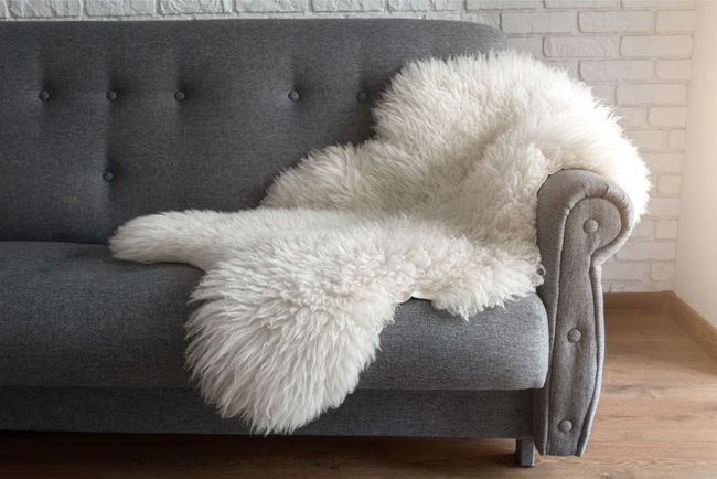 Ein graues Sofa mit einer weißen Schaffelldecke darauf.