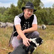 Ein Mann mit Hut kniet neben einem schwarz-weißen Hund.