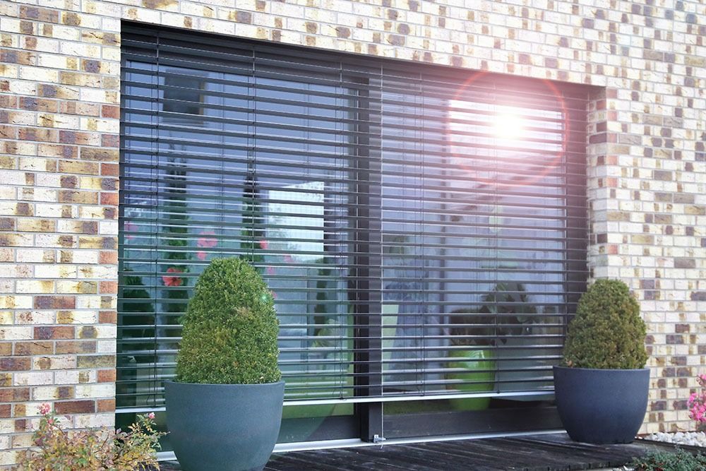 Ein Backsteingebäude mit einem großen Fenster mit Jalousien und Topfpflanzen davor.