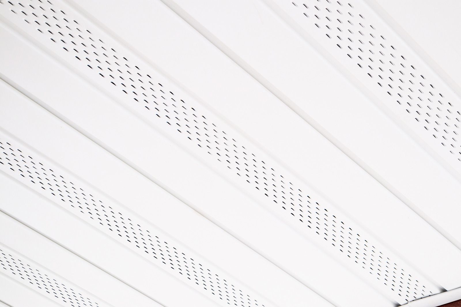 White diagonal slatted ceiling with small perforation holes and shadowed gaps
