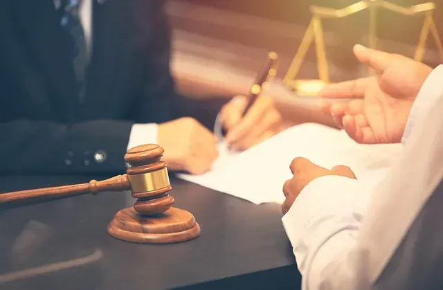 Abogado en el escritorio con un mazo, balanza de la justicia y persona firmando un documento.