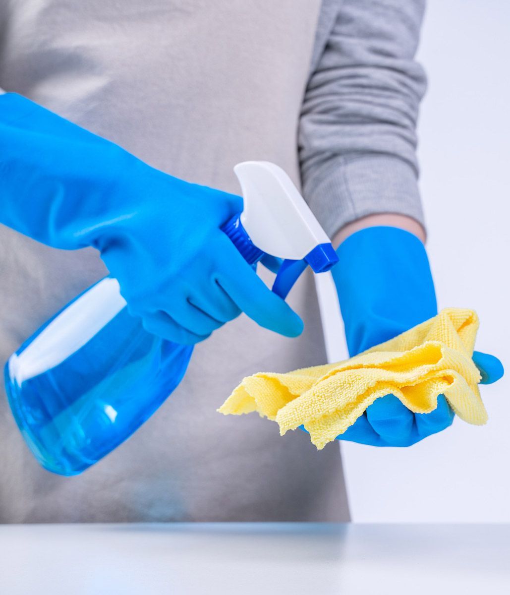 Una persona que lleva guantes azules sostiene una botella de spray y un paño.