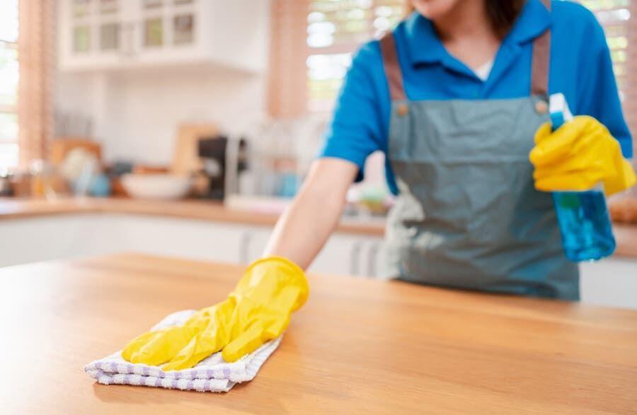 Una mujer que lleva guantes amarillos está limpiando una mesa de madera en una cocina.
