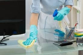 Una mujer con guantes azules está limpiando un escritorio de cristal en una oficina.
