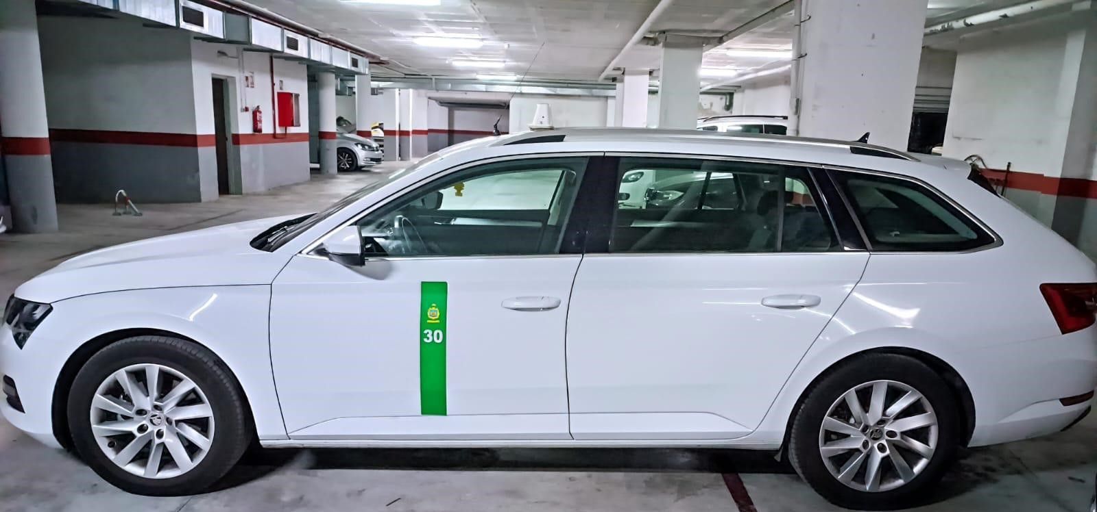 Una fila de taxis esperando en un estacionamiento, con un letrero verde brillante que dice 