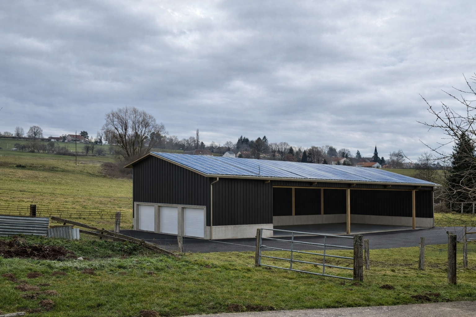 Grange rurale au toit bleu, située à côté d'un champ boueux sous un ciel nuageux