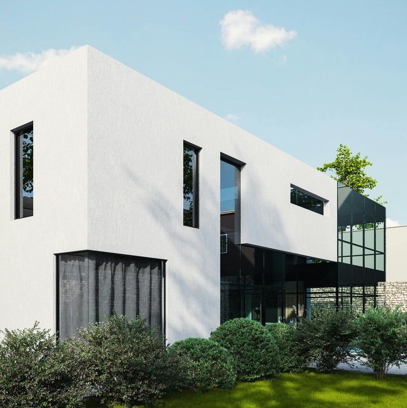 Maison blanche moderne de deux étages, aux encadrements de fenêtres sombres, aux murs de verre et entourée de buissons verts