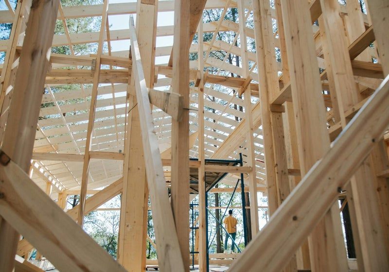 Une personne se tient à l'intérieur de la charpente en bois apparente d'un bâtiment en construction