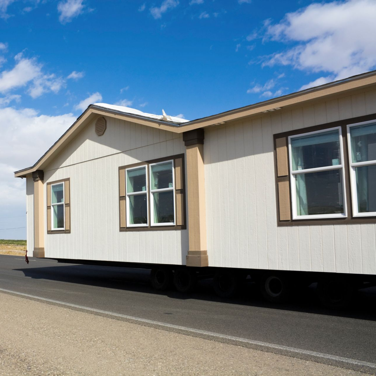 Une caravane blanche est transportée sur une route avec un ciel bleu en arrière-plan.