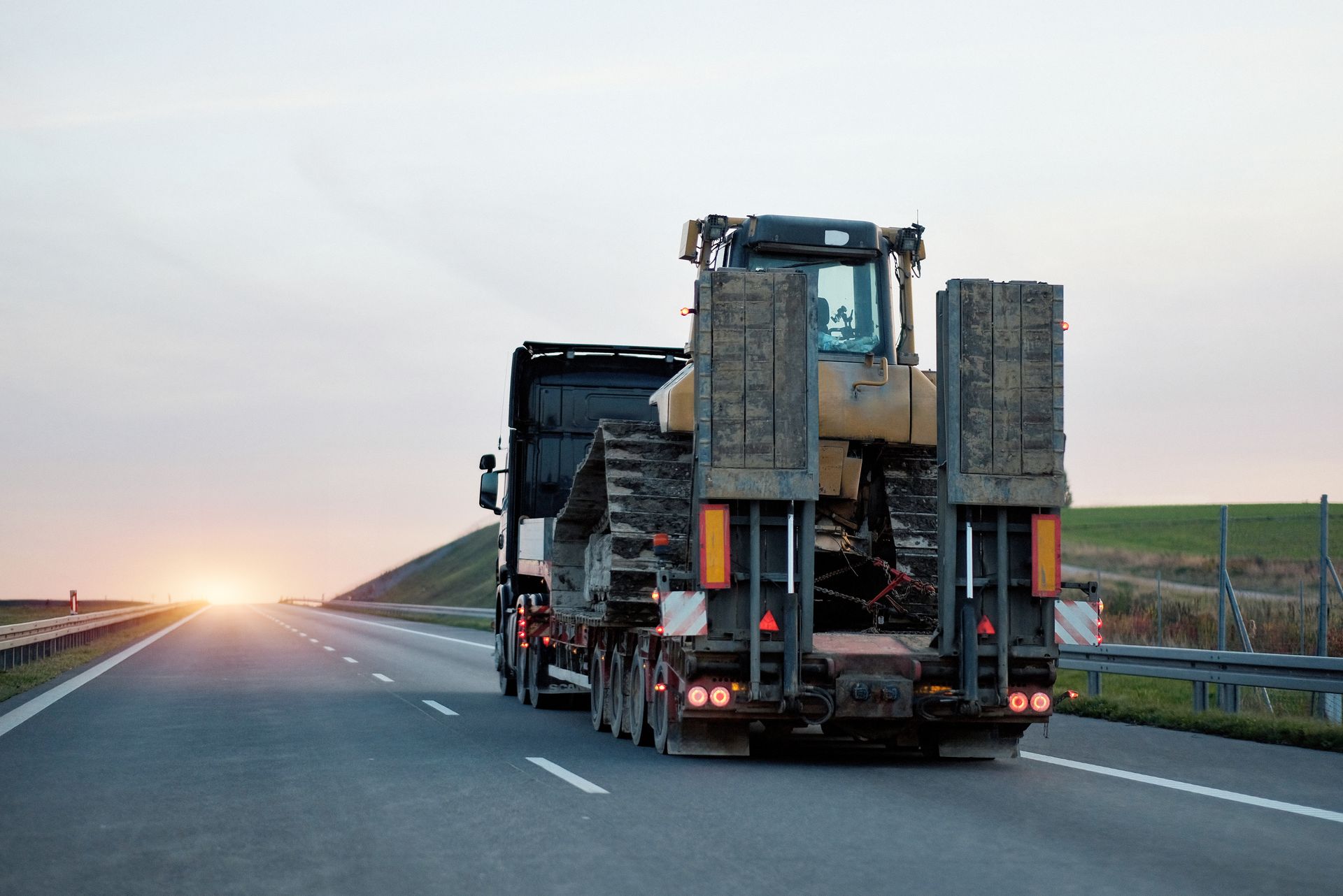 Un bulldozer chargé sur un camion plateau circulant sur une autoroute au crépuscule.