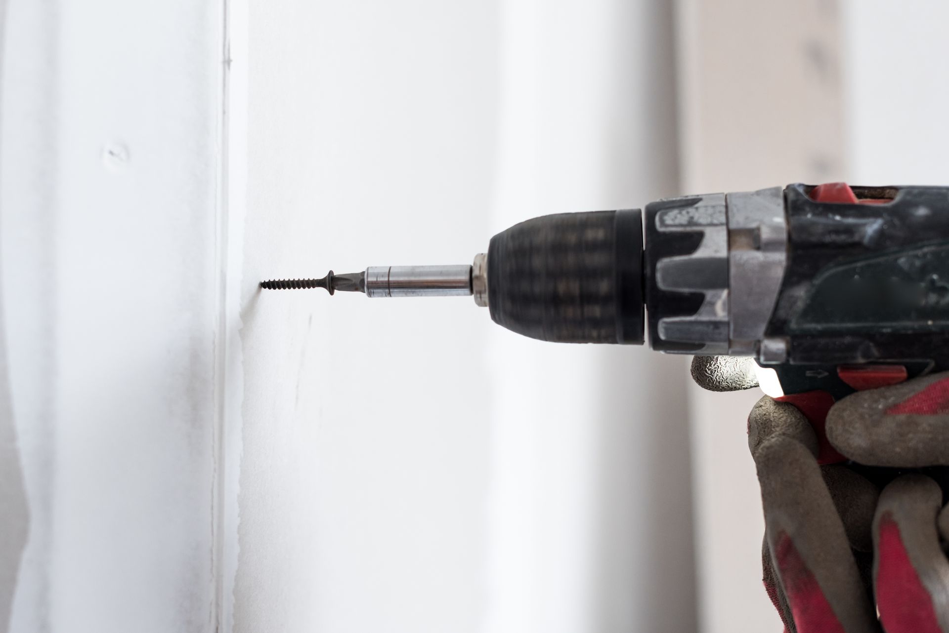 Une perceuse perce un trou dans un mur blanc ; une main gantée tient la perceuse.
