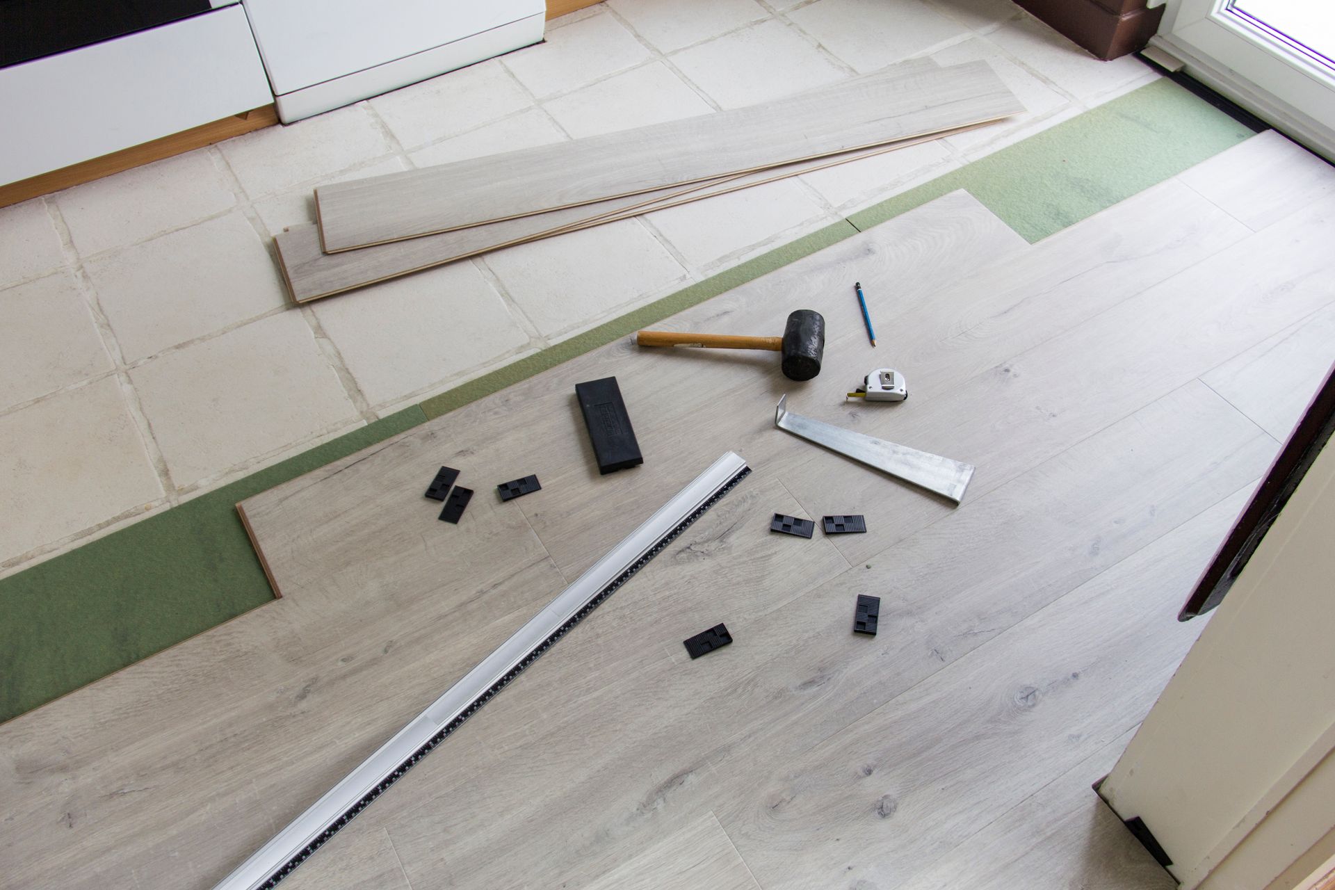 Pose de parquet stratifié en cours. Outils et lames au sol. Présence de beige et de vert.