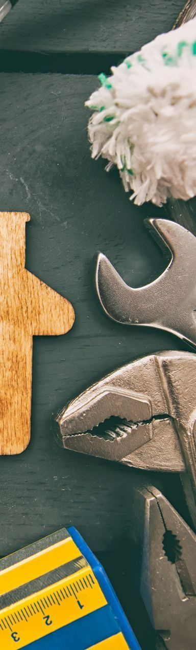 Outils sur une surface sombre : clé, pince, tournevis, ruban à mesurer jaune et bleu, et un chiffon.