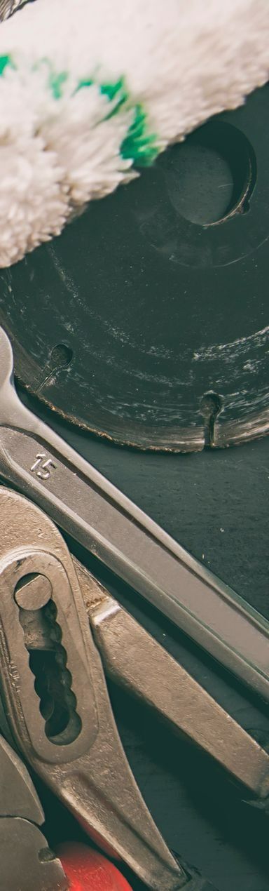 Sur une surface sombre, on aperçoit des outils : une clé, une pince et une lame de scie circulaire.