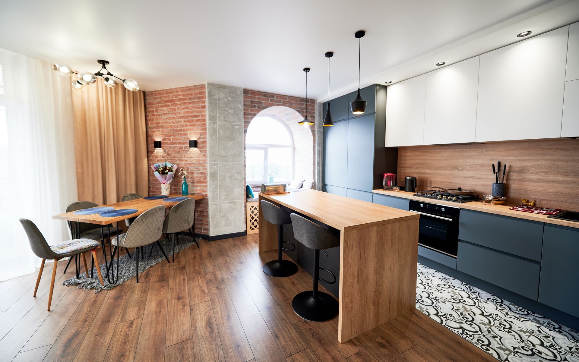 Cuisine moderne avec îlot en bois, mur en briques, placards foncés et coin repas.