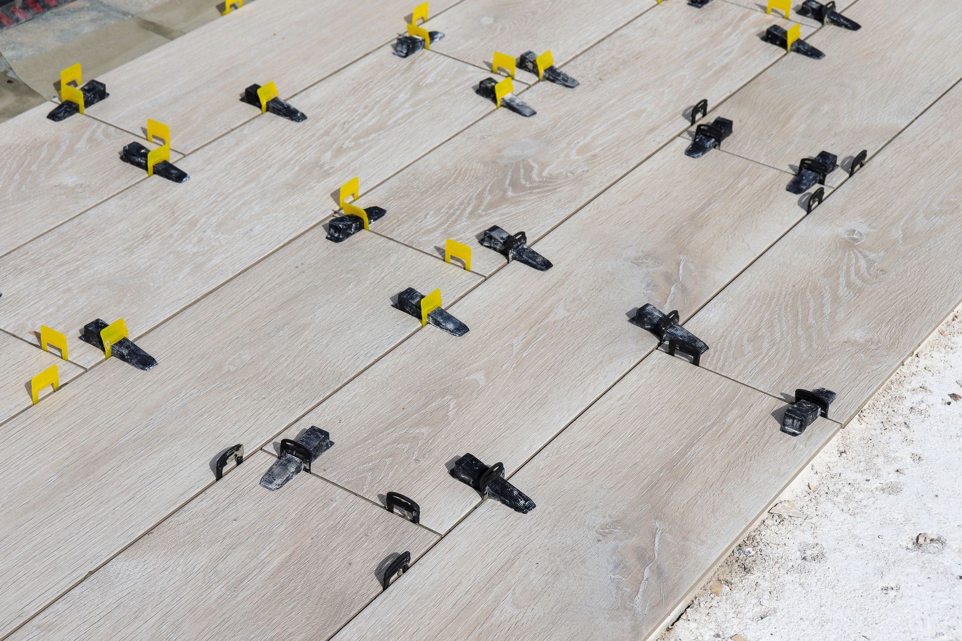 Gros plan sur des planches imitation bois avec des clips de nivellement pour carrelage jaunes et noirs, montrant la construction en cours.