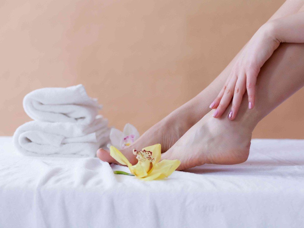 Los pies de una mujer están sentados sobre una mesa junto a una flor y toallas.
