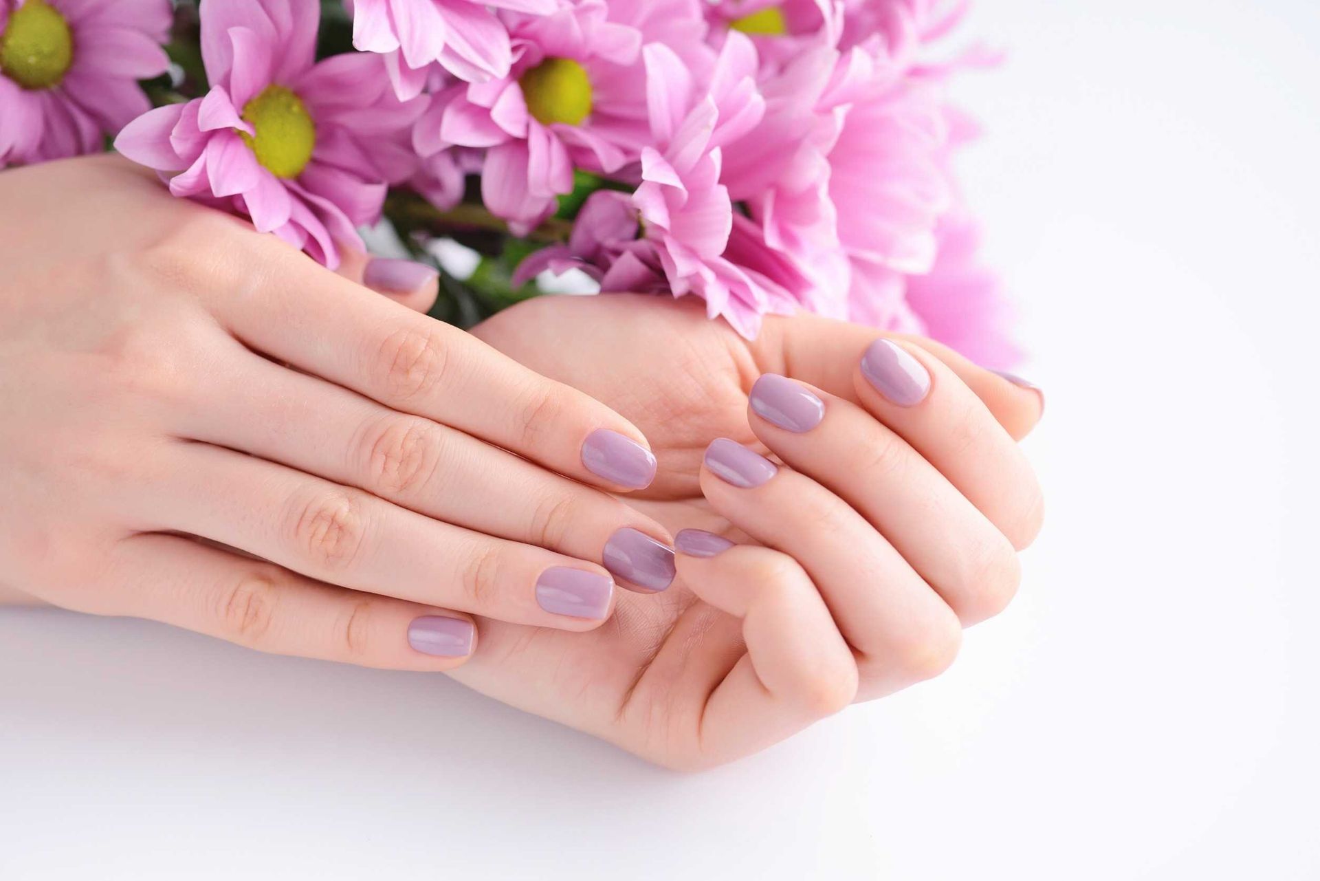 Las manos de una mujer con uñas moradas sostienen un ramo de flores rosas.