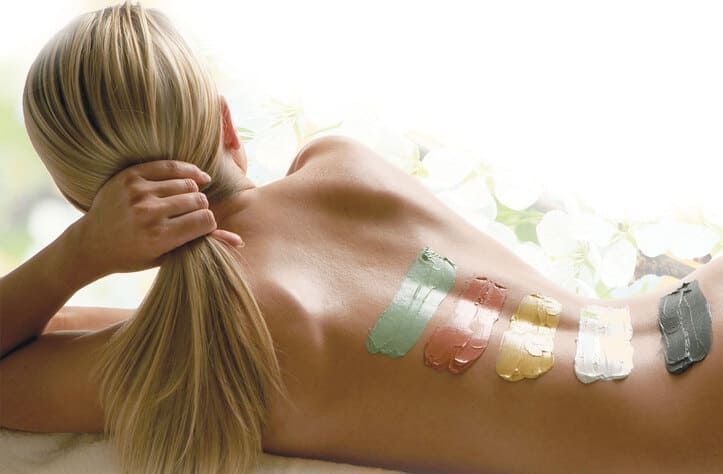 Una mujer está acostada en una cama con un montón de pintura de diferentes colores en la espalda.