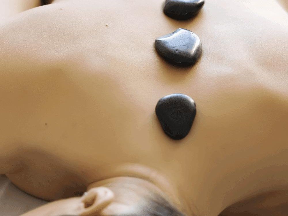 Una mujer está recibiendo un masaje con piedras calientes en la espalda.
