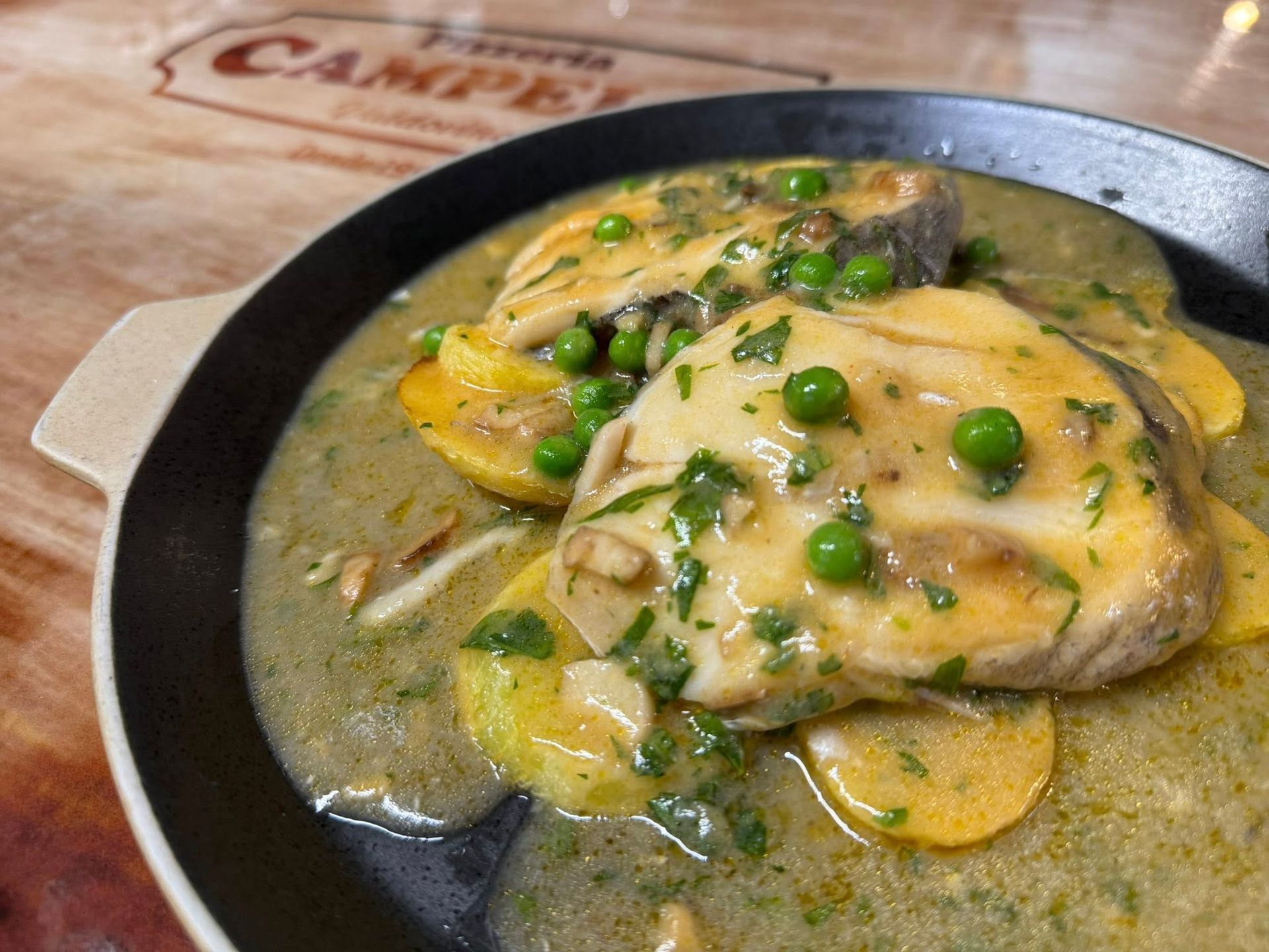 Guiso de pescado con guisantes y patatas en una sartén negra sobre una mesa de madera.