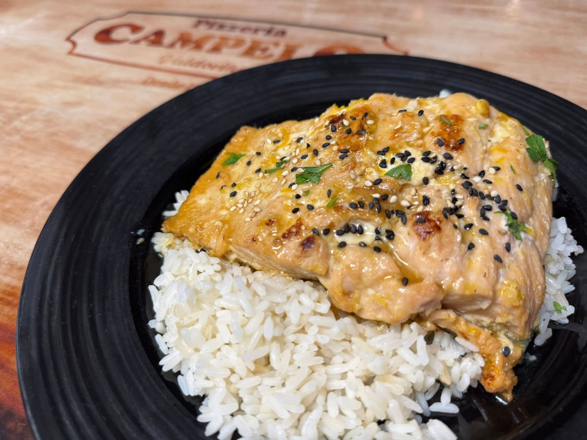 Filete de salmón con semillas de sésamo sobre arroz blanco en un plato negro.
