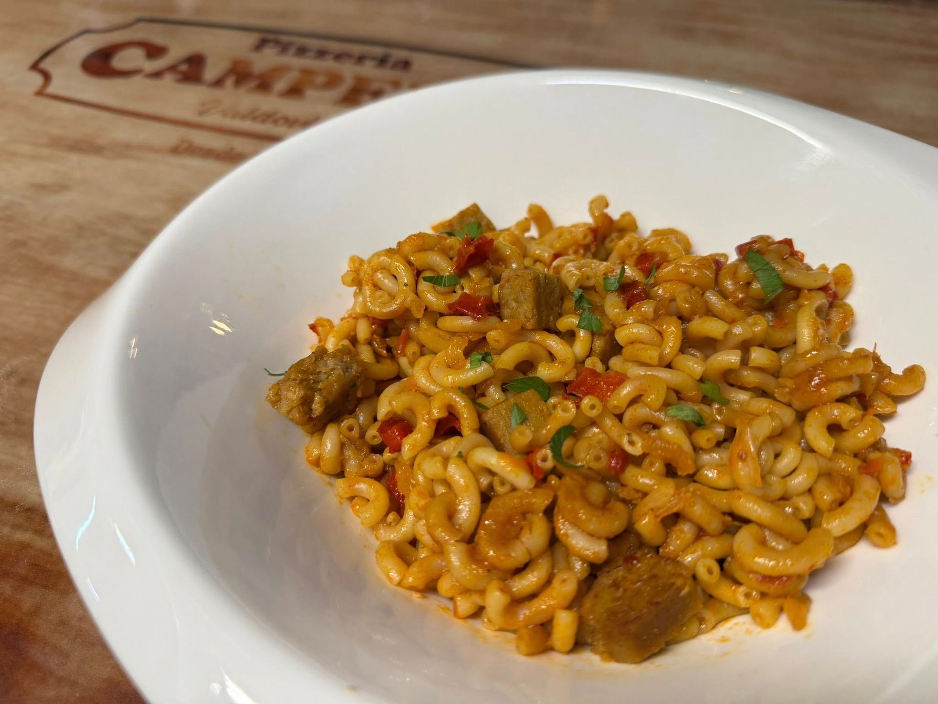 Plato de pasta con salchicha, pimientos rojos y hierbas en un tazón blanco.