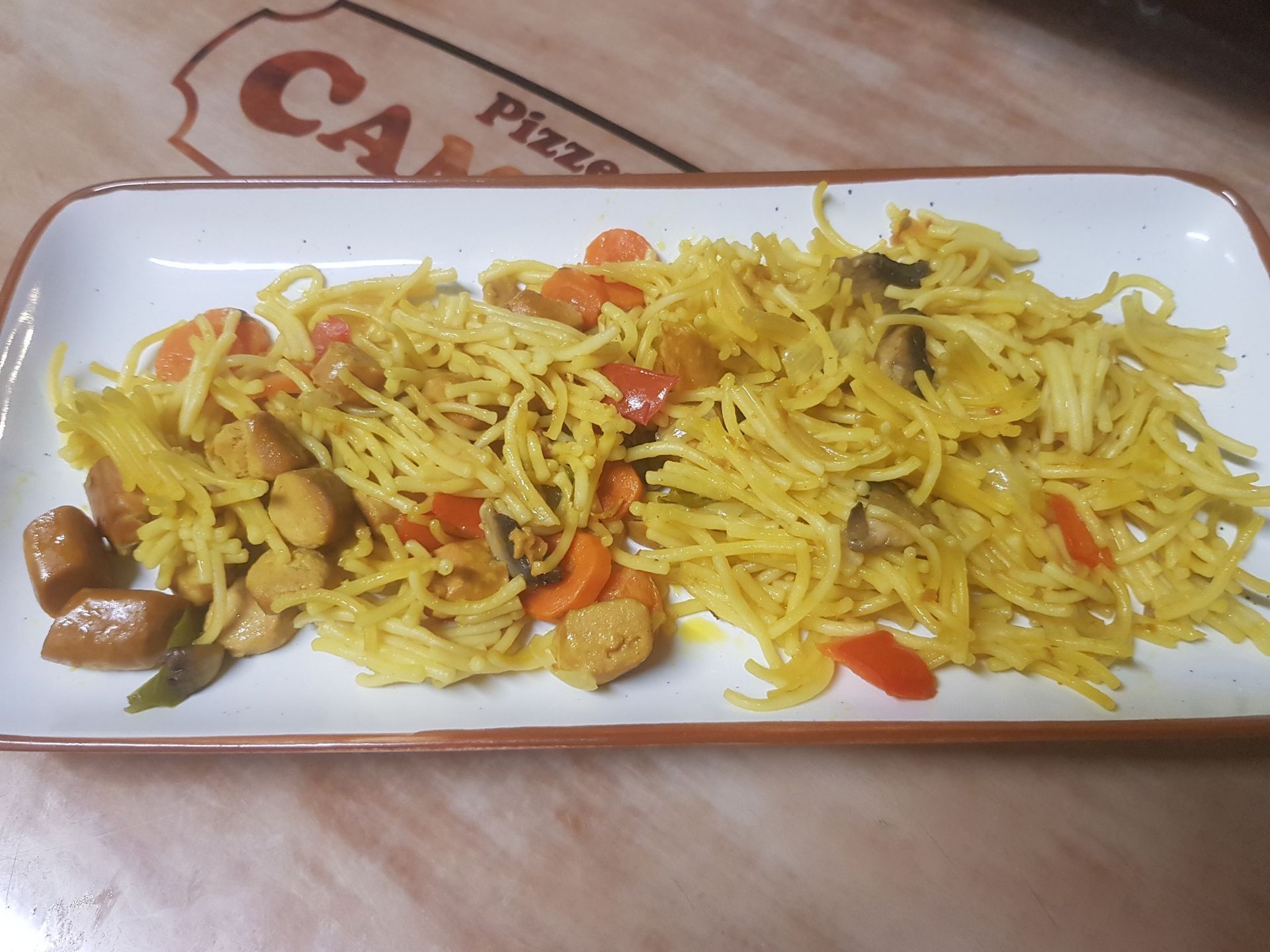 Plato de pasta con verduras y carne en plato rectangular.