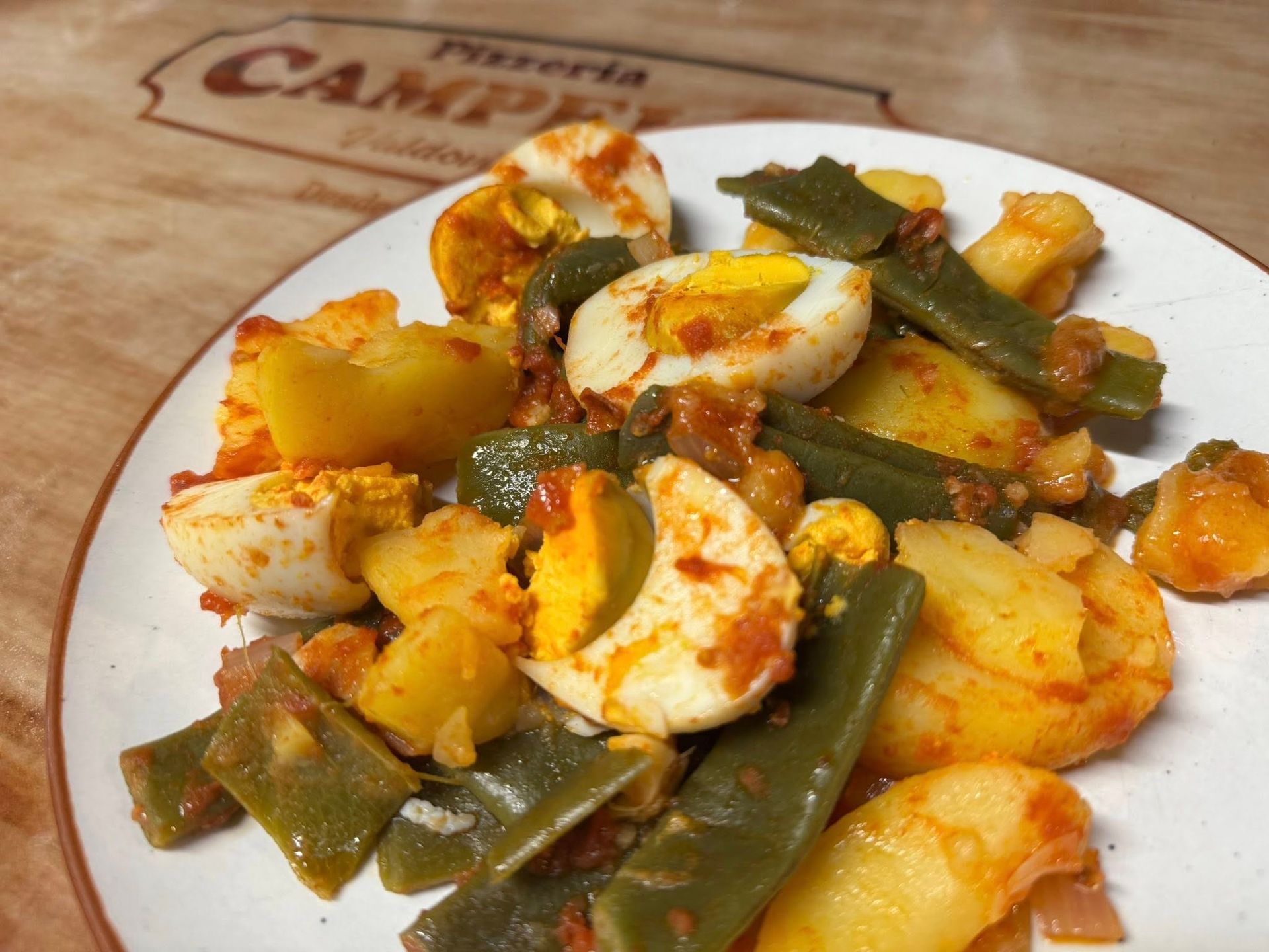 Plato de comida: huevos cocidos, patatas, judías verdes y salsa a base de tomate.
