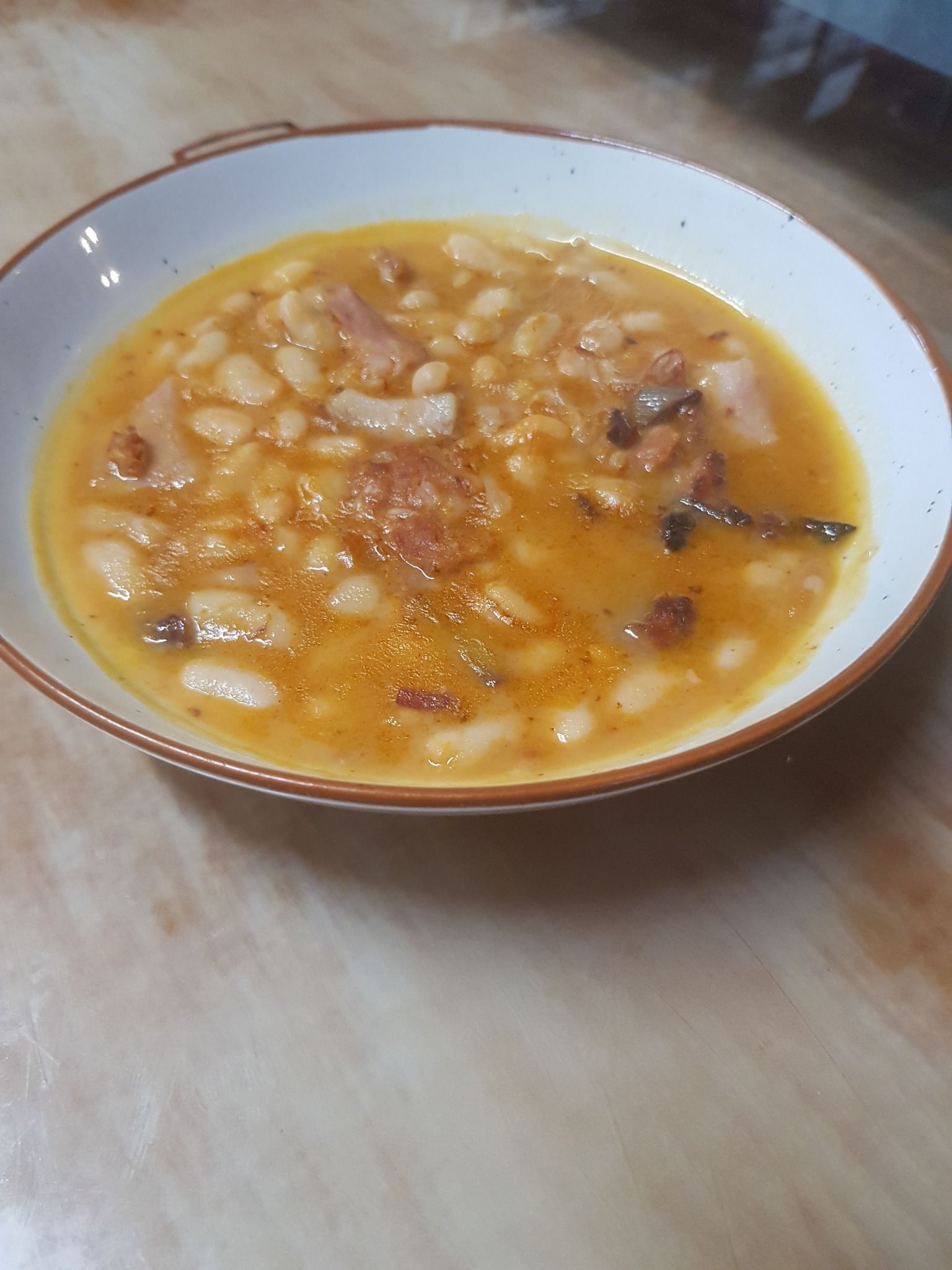 Plato de guisado de judías blancas con carne en caldo de color crema.