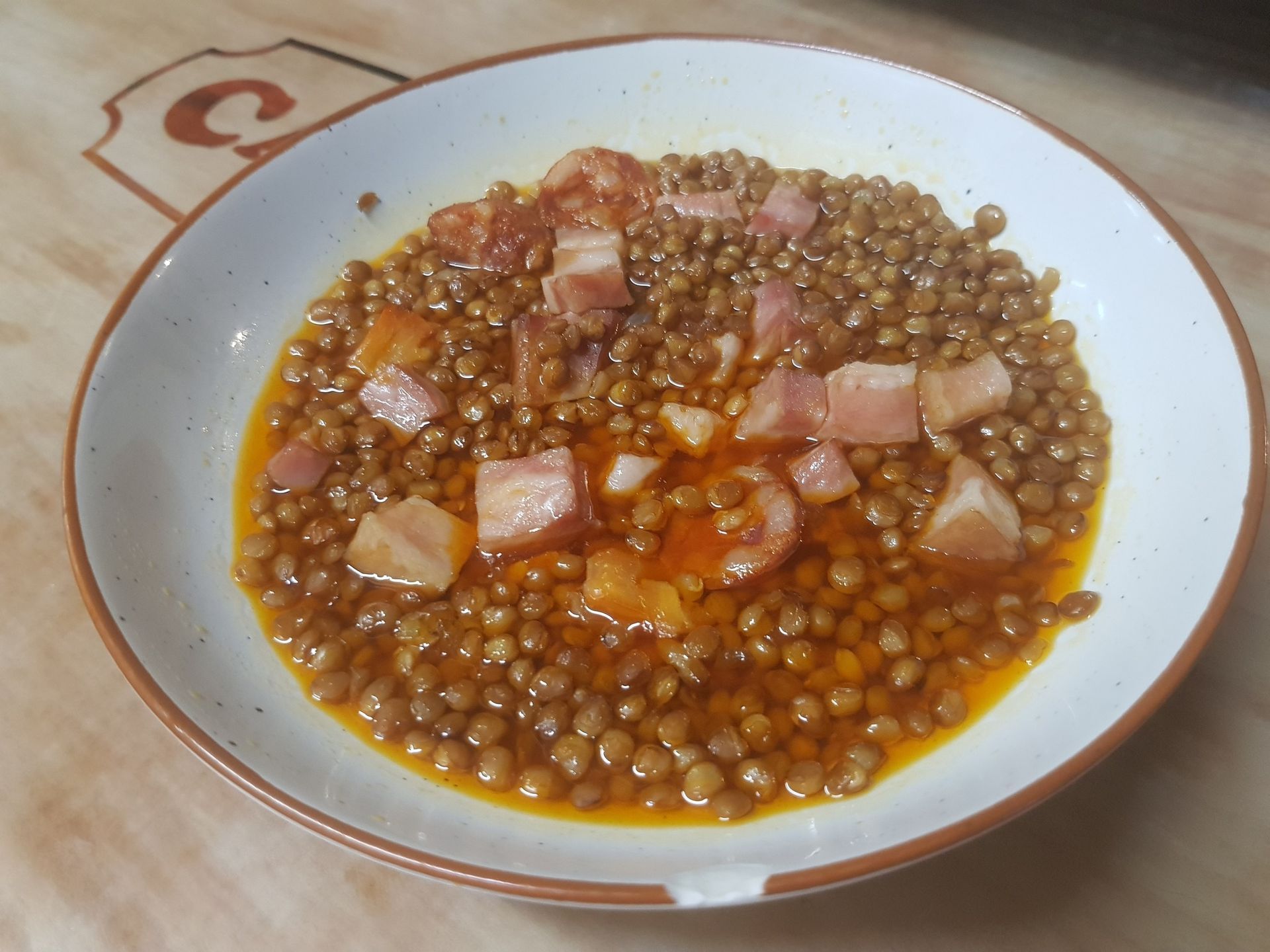 Lentejas con carne cortada en cubos y salsa en un recipiente blanco, sobre una superficie de madera.