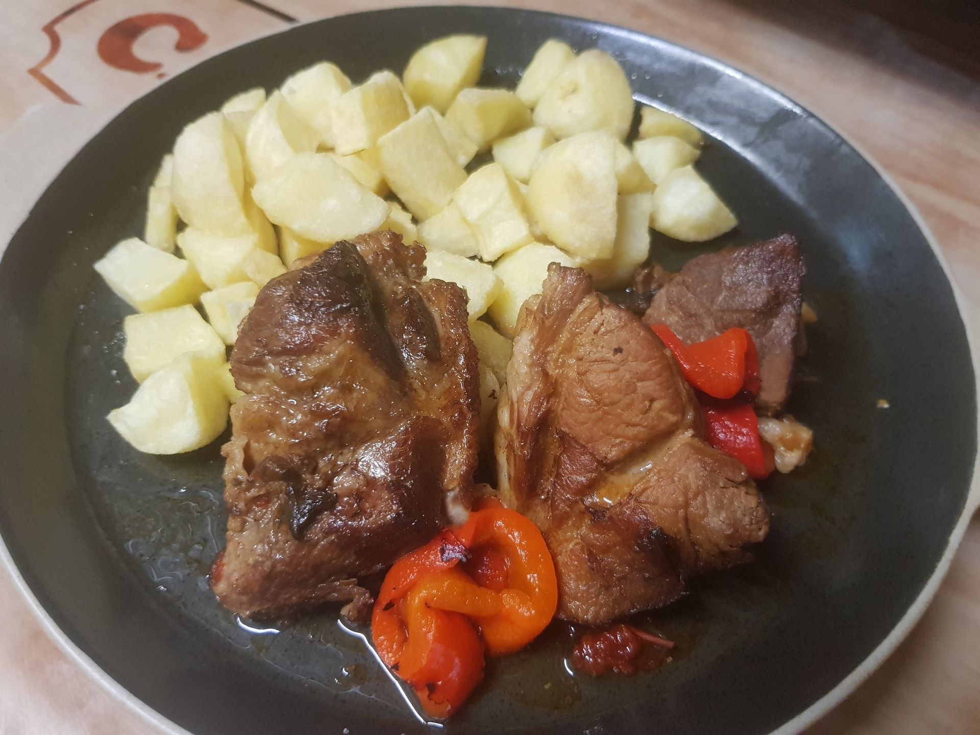 Plato de filetes de cerdo cocidos y pimientos rojos asados con patatas cortadas en cubos.